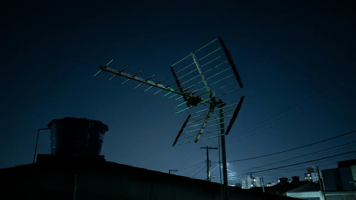Antena digital UHF instalada no telhado de uma casa brasileira contra o céu azul-escuro do fim de tarde.