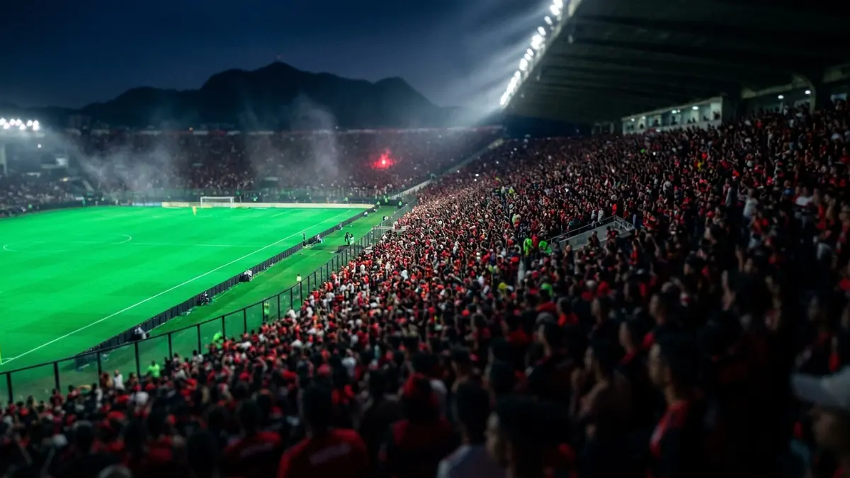 Arquibancada lotada em vermelho e preto num estádio do Rio de Janeiro à noite, com o gramado iluminado ao fundo.
